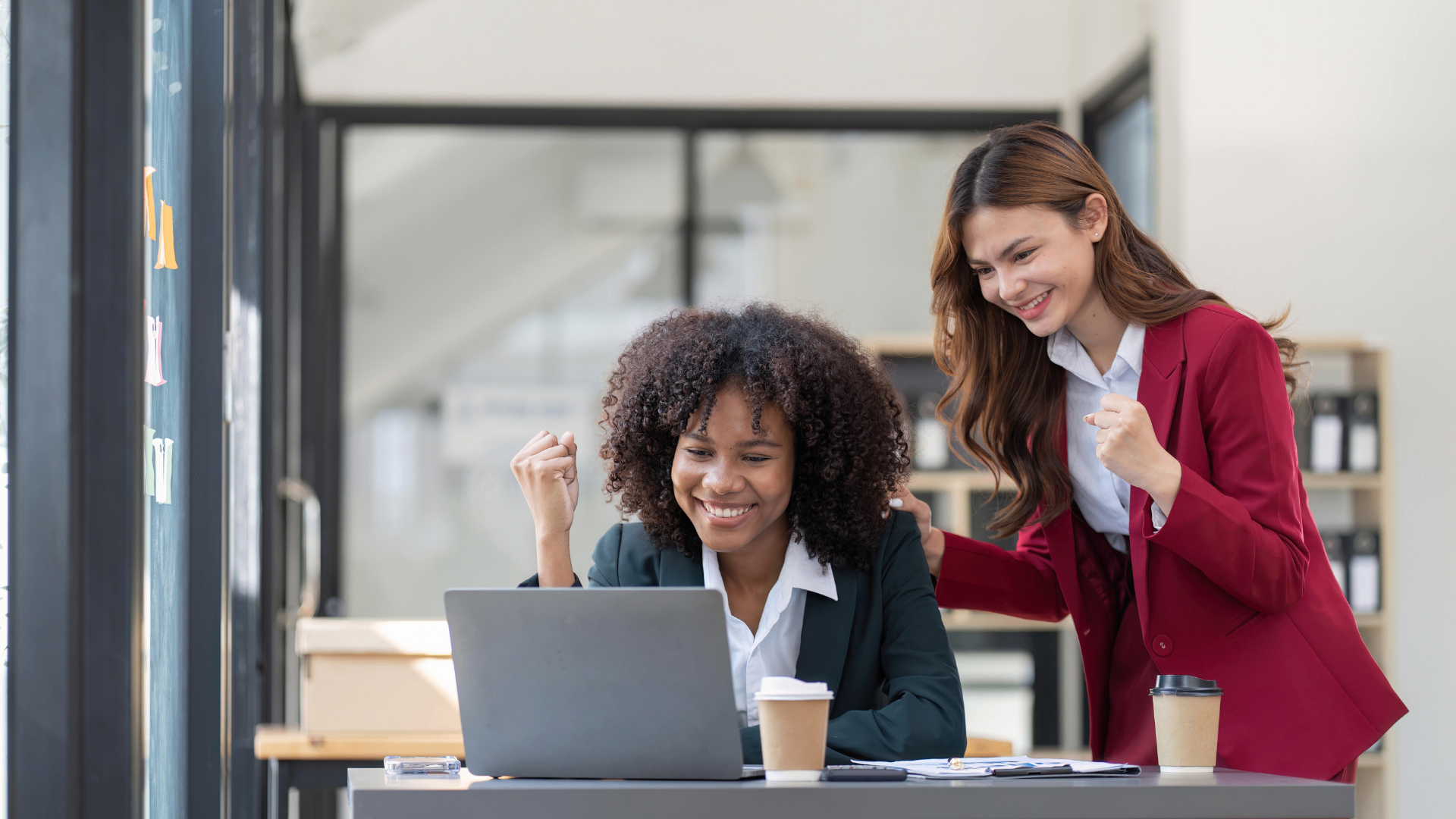 Two businesswomen celebrating great customer service results at a laptop