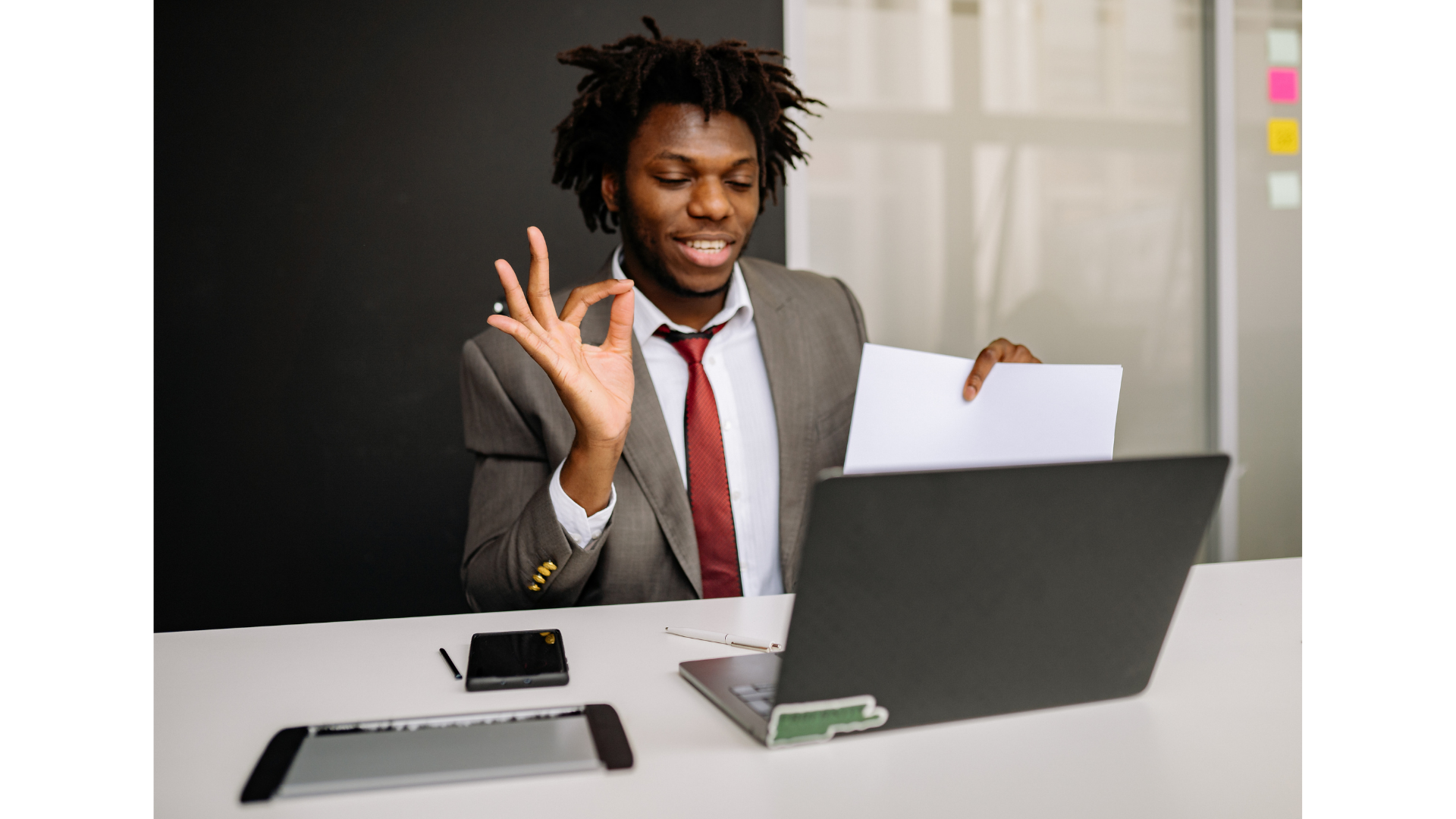 Business professional making an OK gesture while reviewing documents at a laptop
